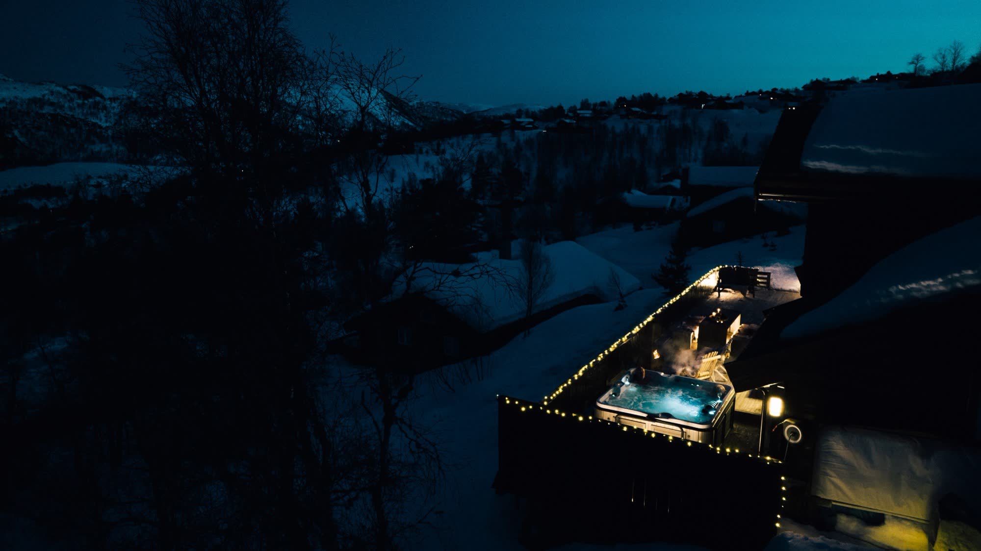 A lit, steaming hot tub on a snowy deck at night